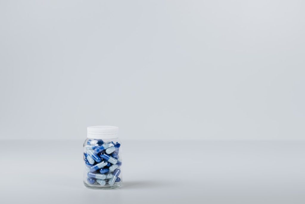 A jar filled with blue and white capsules on a plain background